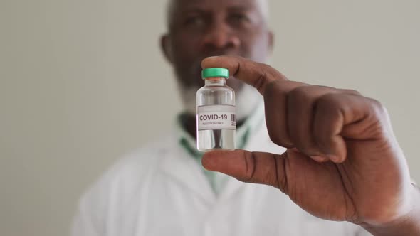 Close up of male african american doctor holding vaccine bottle at hospital