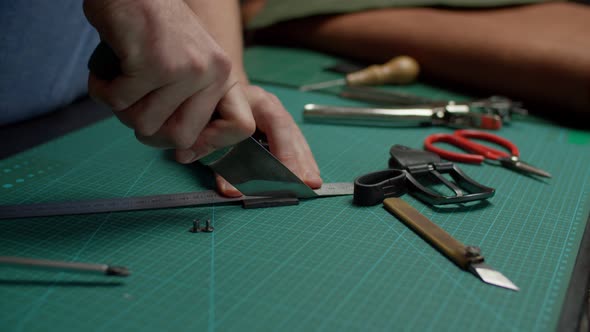 Artisan Using Utility Knife Cutting Off Belt Length By Hand Indoors