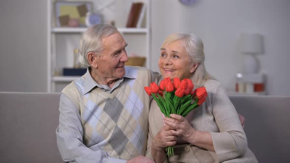 Elderly Man Hugging Happy Woman With Bunch of Tulips, Present From Beloved