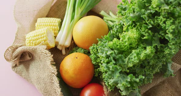 Video of fresh fruit and vegetables in rustic bag over pink background