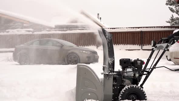 Villager removes snow with snowblower in yard at snowfall in slow motion