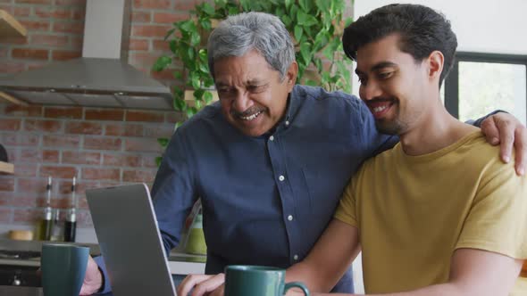 Smiling biracial man with arm around young son using laptop at home