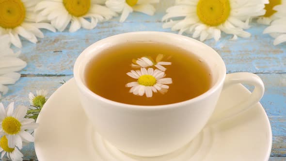 Composition with chamomile flowers and white cup of herbal tea. Summer theme.