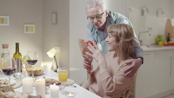 Senior Man Giving Flowers to Wife at Romantic Dinner