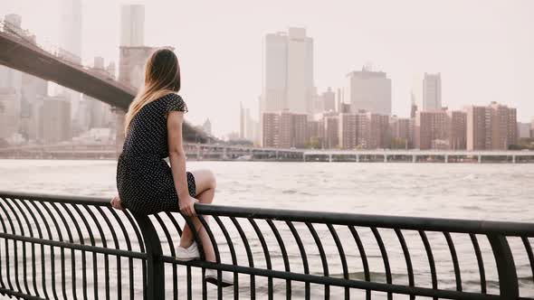 Beautiful European Girl Sitting on River Embankment Fence, Looking Back at Camera Smiling Near