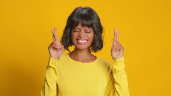 Happy Woman Makes Wish and Crosses Fingers for Good Luck Over Yellow Background