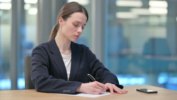 Beautiful Young Businesswoman Writing on Paper in Office
