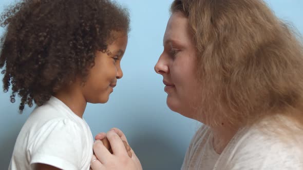 Side View of Caucasian Mother and Mixed Race Daughter Looking at Each Other Isolated Over Blue