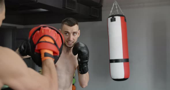 Fighter in Boxer Gloves is Practising His Strikes with Trainer in Slow Motion in the Gym Kickboxers