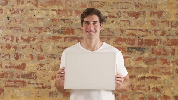 Caucasian man holding a white rectangle on a brick wall