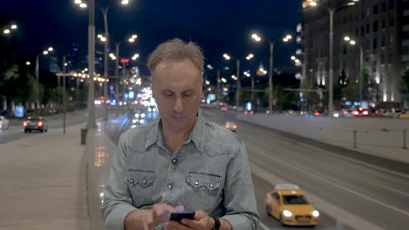 Middle Aged Man Uses Smartphone at Parapet in Evening City