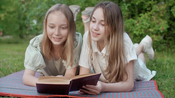 Happy Young Girls Lying and Reading Book in Park