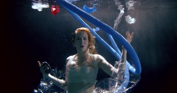 Woman Is Swimming Underwater Between Plastic Garbage, Tape, Cups, Tubes