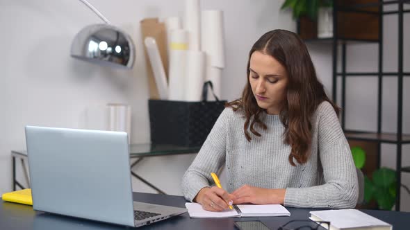 Concentrated Business Woman with a Laptop Writing Down