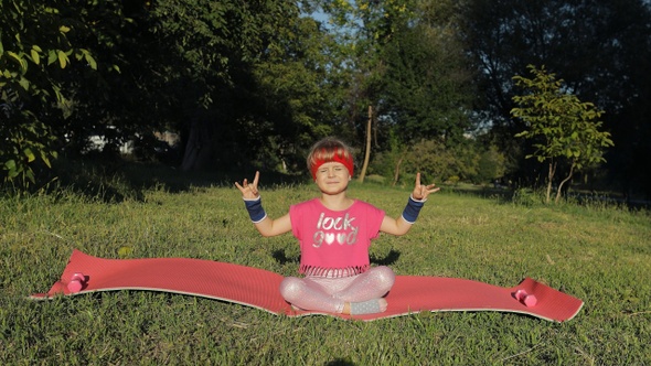 Child Sitting on Mat and Performing Yoga Meditation Outdoors in Park. Girl Doing Yoga Exercises