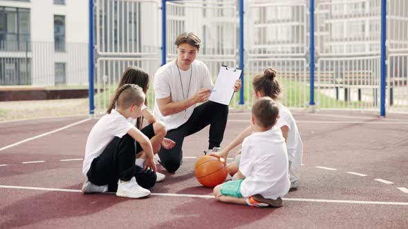 Male Coach Emotionally Explaining Game Plan to Young Basketball Players on Basketball Court