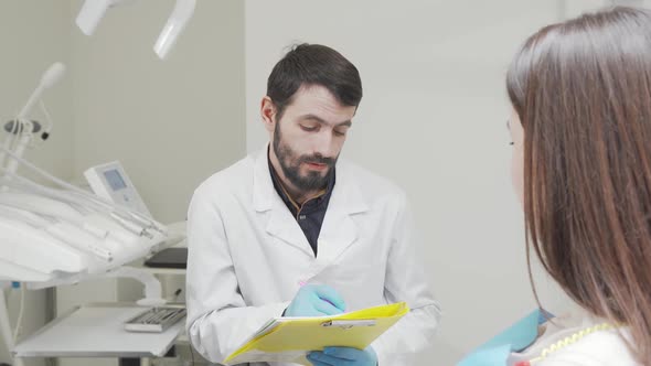 Bearded Dentist Filling Medical Documents While Talking to Patient