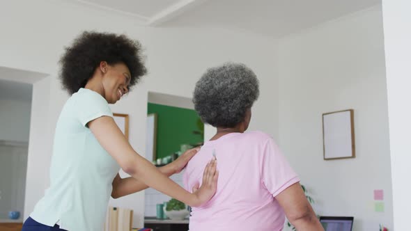 African american female physiotherapist wearing face mask helping senior female patient exercise