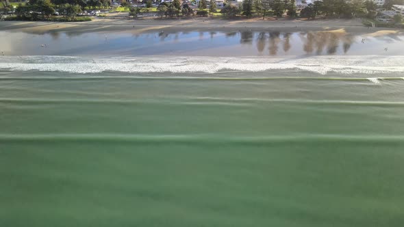 Drone pan up of relaxing waves along the beach at sunset