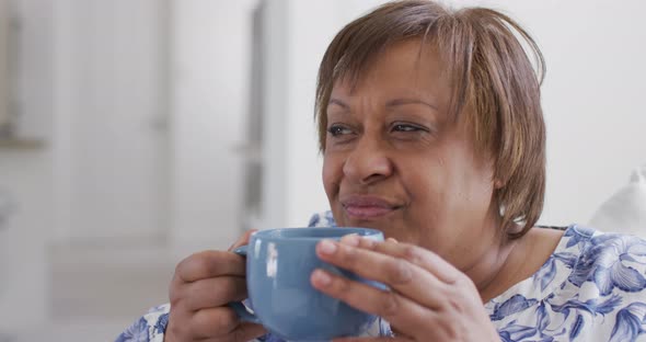 Happy african american senior woman enjoying drinking cup of tea, looking away smiling