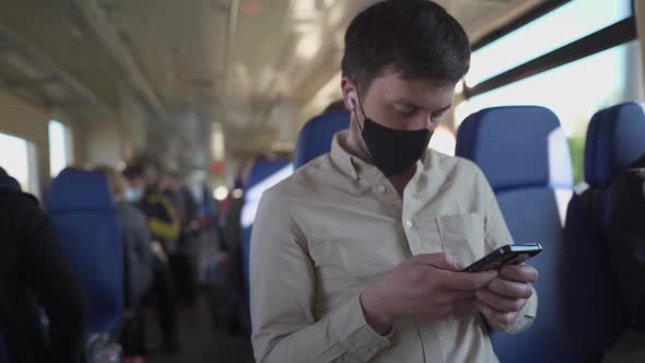 Man Passenger in Face Mask and Headphones Using Phone for Online Watching Video and Reading News