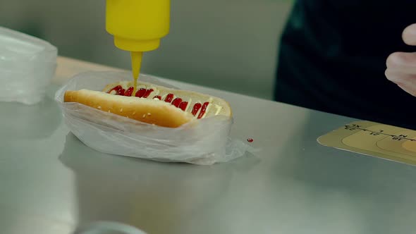CU Slow Motion Cook Is Preparing a Hot Dog Watering It with Mustard