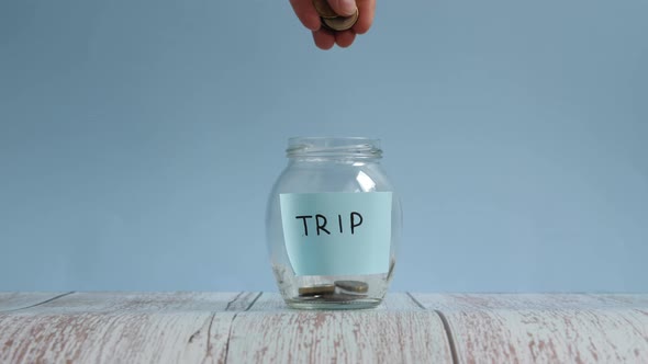 Saving money for trip. Putting coins into glass jar