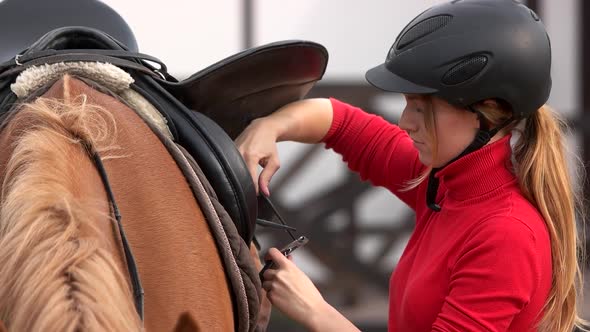 Young Woman Saddles a Horse Outdoors