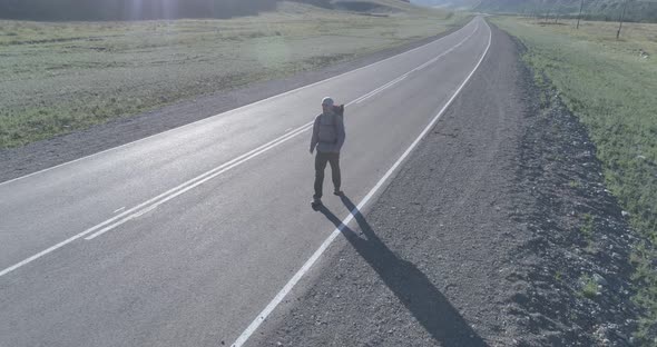 Flight Over Hitchhiker Tourist Walking on Asphalt Road. Huge Rural Valley at Summer Day. Backpack