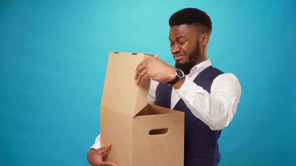 Young African Man Opens Carton Box Dislike What's in It Against Blue Background