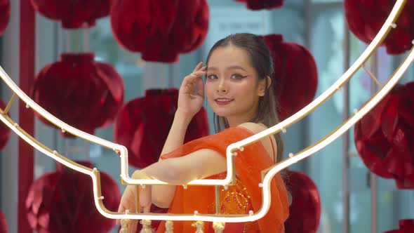 Asian woman with traditional red dress and makeup poses by the paper lanterns as she celebrates the