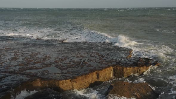 Waves crashing on the cliffy coastline in Portland, England, at dusk