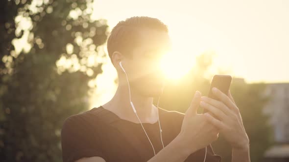 Young Man Enjoys Listening to Music on Headphones Using His Smartphone at Sunset in the City
