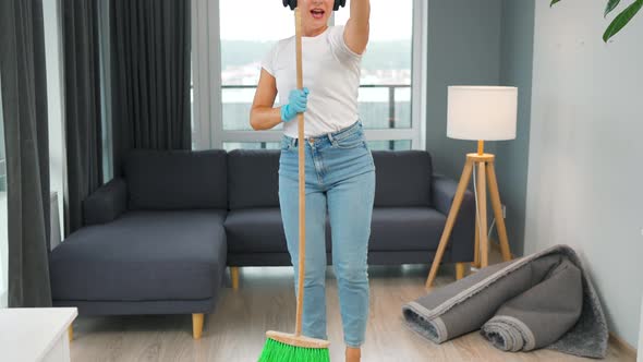 Woman in Headphones Cleans the House and Have Fun Singing with a Broom Like a Star at a Concert