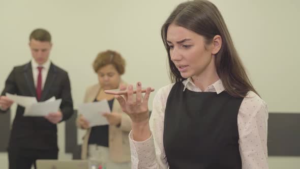 Portrait of Angry Young Woman in Formal Wear Speaks By Her Cellphone in the Foreground in the Office