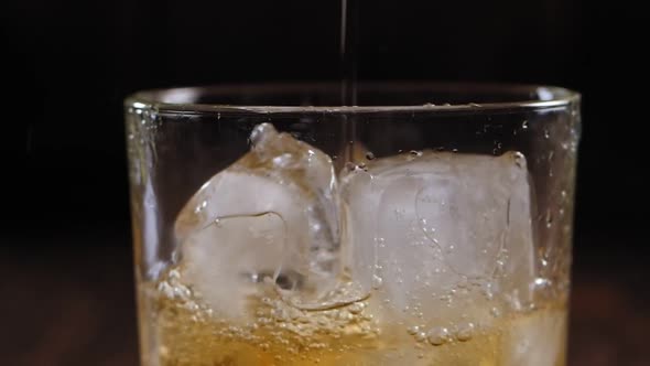 Close-up of Whiskey Poured Into a Glass with Ice on a Brown Wooden Background