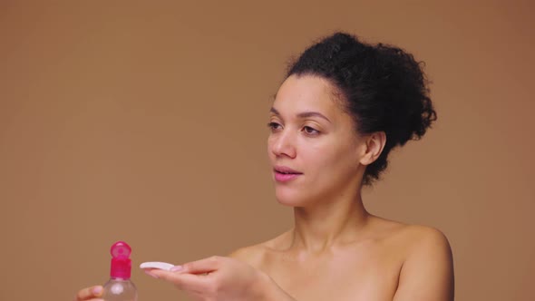 Beauty Portrait of Young African American Woman Pouring Lotion Onto Cotton Pad and Cleansing Face