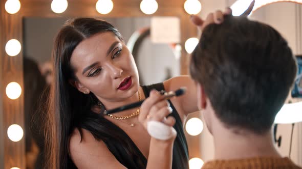 Woman Make Up Artist Applying Base on the Face of Male Model with a Brush