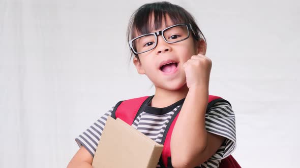 Smiling schoolgirl wearing summer outfit with backpack holding books on white background in studio.