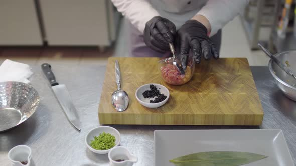 Chef in Black Rubber Gloves Preparing Dish with Raw Tuna and Salmon in Modern Restaurant Kitchen