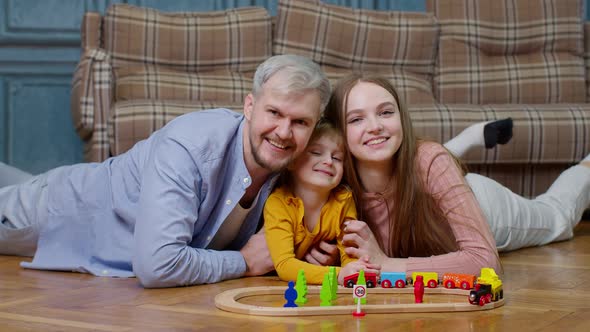 Young Mother and Father Playing with Child Daughter Riding Toy Train on Wooden Railroad Game at Home