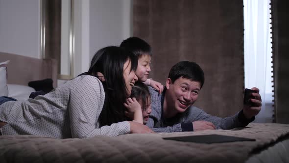 Smiling Chinese Family Taking Selfie Lying on Bed