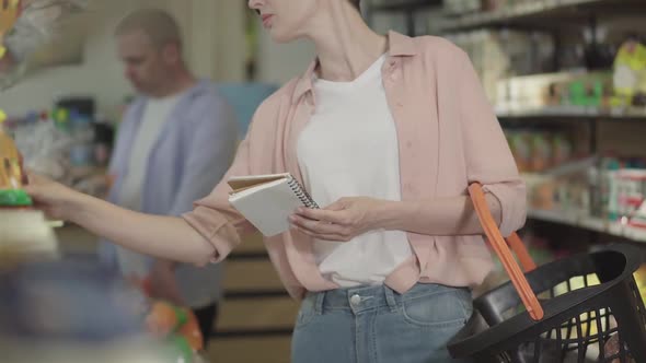 Unrecognizable Woman with Shop List Making Purchases in Grocery. Young Caucasian Female Buyer Taking