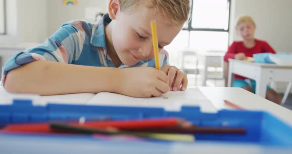 Video of happy caucasian boy sitting at school desk and writing