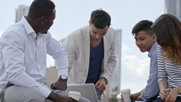 Man Explaining Colleagues Something on Laptop Outdoors
