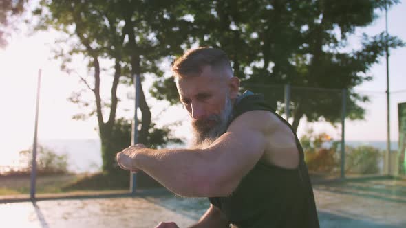 Middle Aged Man with Long Gray Beard Boxing with Shadow on Basketball Court During Sunrise Shaky