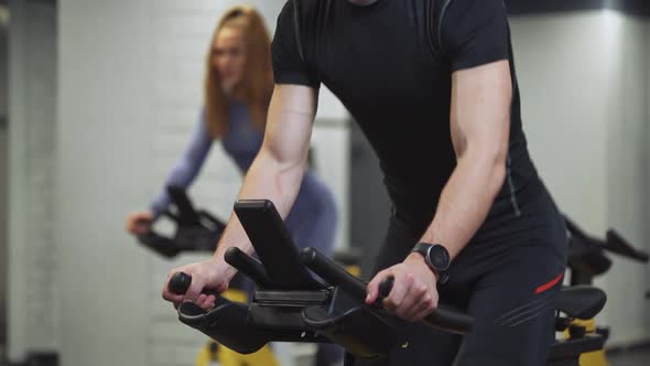 Man and Woman Training on a Spin Bikes Performs Aerobic Endurance Training on the Simulators in the