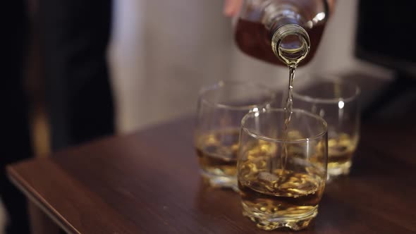 Barman Pouring Golden Whiskey Cognac Brandy From Alcohol Bottle Into Glasses on Wooden Table