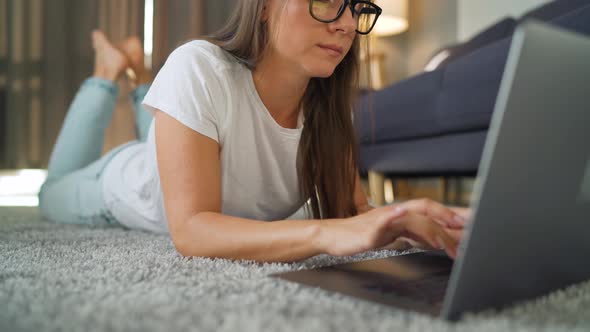 Woman with Glasses Is Lying on the Floor and Working on a Laptop. Concept of Remote Work.