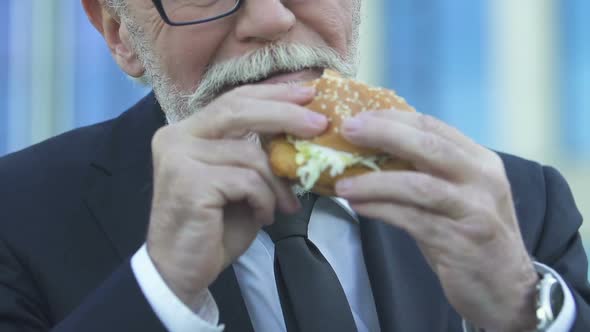 Old Businessman Eating Tasty but Fatty Hamburger, Unhealthy Food, Closeup